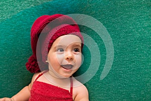 Cute newborn baby in the red hat. Happy baby on a green background. Closeup portrait of newborn baby. Baby goods packing template.