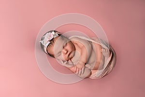 Cute newborn baby is sleeping, with flowers. On a pink background