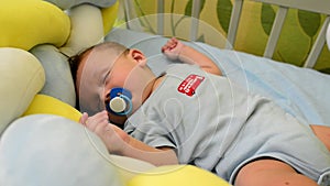 Cute newborn baby toddler boy sleeping in his infant bad and sucking on a pacifier