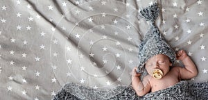 Cute newborn baby in warm hat sleeping on bed, top view with space for text. Banner design