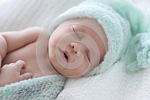 Cute newborn baby in warm hat sleeping on plaid, closeup