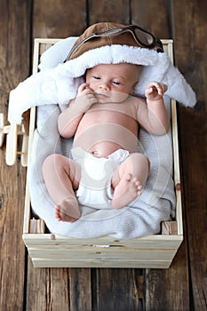 Cute newborn baby wearing aviator hat in crate, top view