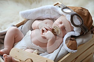 Cute newborn baby wearing aviator hat with toy sleeping in crate