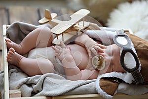 Cute newborn baby wearing aviator hat with toy sleeping in crate