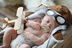 Cute newborn baby wearing aviator hat with toy sleeping in crate