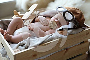 Cute newborn baby wearing aviator hat with toy sleeping in crate