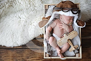 Cute newborn baby wearing aviator hat with toy sleeping in wooden crate. Space for text