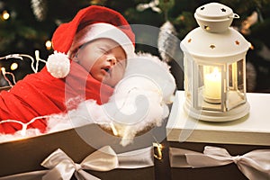 Cute newborn baby wearing Santa Claus hat is sleeping in the Christmas gift box