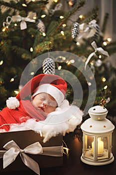 Cute newborn baby wearing Santa Claus hat is sleeping in the Christmas gift box
