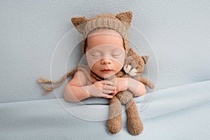 A cute newborn boy in the first days of life sleeps in a brown hat with cat ears