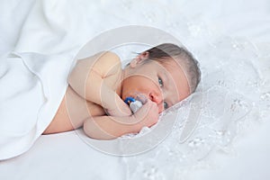 Cute newborn boy girl with baby's dummy on background of white l