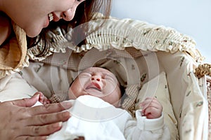 Cute newborn infant baby boy lying down on beautiful crib basket on bed, little child sleeping, mother gentle touching him, lovely