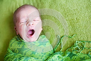 Cute newborn in light green wrap sleeps and yawns on green background