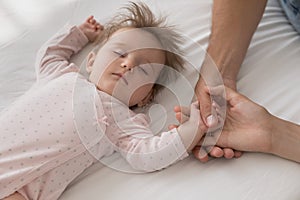 Cute newborn sleeping on bed touch loving parents hands