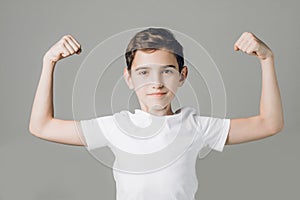 Cute nice boy in white T-shirt shows biceps isolated on grey background