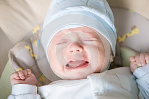 Cute nice little baby boy crying lying  on bed at home.