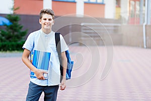 Cute, nice, young 11 years old boy in blue shirt stands with workbooks and backpack in front of his school. Education