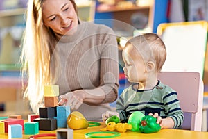 Cute nursery teacher and child toddler playing educational toys in kindergarten