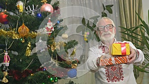 Cute old man holds Christmas presents near the Christmas tree