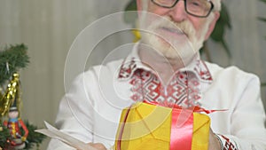 Cute old man stands near the Christmas tree with presents