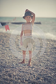 Cute old style boy kid on beach walking posing wearing fancy shorts with gallows and gentleman hat enjoy summer time alone on awes