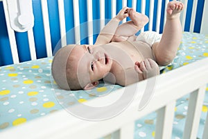 Cute one month old newborn baby is laying on her back in the crib, crying.