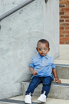A cute one year old toddler almost preschool age African-American boy with big eyes sitting on city steps