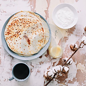 Stack of delicious homemade pancakes on plate with honey, sour cream and tea. Breakfast. Rustic style, close up top view. Flat lay