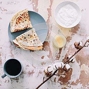 Stack of delicious homemade pancakes on plate with honey, sour cream and tea. Breakfast. Rustic style, close up top view. Flat lay