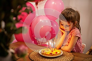 Cute pensive little girl looking at her birthday cake