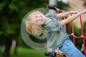 Cute perky preschooler boy having fun on outdoor playground. Spring or summer or autumn active sport leisure for kids. Outdoor photo