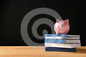 Cute piggy bank on stack of books against dark background