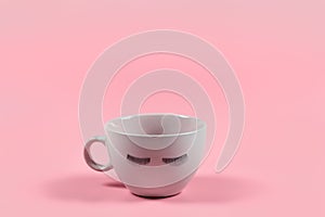 Cute pink coffee or tea mug with false lashes on a pink background with copy space.