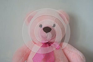 A cute pink teddy bear sits against a wall