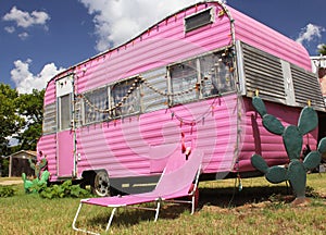 Cute pink travel trailer under a bright cloudy sky with cacti and trees around a tumbona chair photo