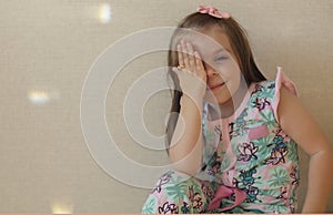 Cute playful little girl covering one eye with hand and smiling at camera