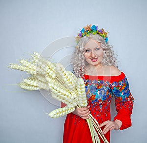 Cute plump girl from the village in a red summer sundress with a sheaf of wheat in her hands on white studio solid background