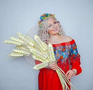 Cute plump girl from the village in a red summer sundress with a sheaf of wheat in her hands on white studio solid background