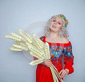 Cute plump girl from the village in a red summer sundress with a sheaf of wheat in her hands on white studio solid background