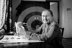 Cute 80 plus year old senior woman using vintage sewing machine. Black and white image of adorable elderly woman sewing clothes.