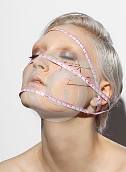 Cute portrait of blonde woman with measure ribbon on head and perforation lines on face, beauty plastic surgery concept