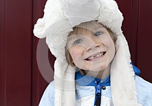 cute portrait of face of preschooler boy with sincere toothless smile in warm fur hat