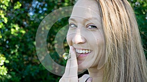 Cute portrait of young blonde woman face smoking daisy flower weed smiling with blue clear eyes isolated in nature