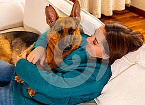 Cute portrait of young woman and dog german shepherd hugging at cozy home in winter