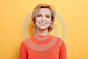 Cute positive girl smiling looking at camera over yellow background.