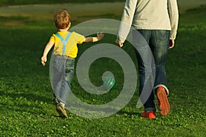 Cute positive kid with mother, playing happily with ball on green meadow