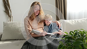 Cute pregnant mom reading a book to her eldest son. Quality parenting time with children.