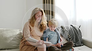 Cute pregnant mom reading a book to her eldest son. Quality parenting time with children.