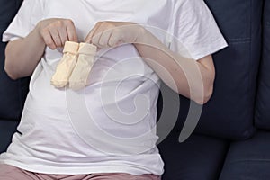 Cute pregnant woman holding socks for newborn. Baby socks on the belly of a pregnant woman