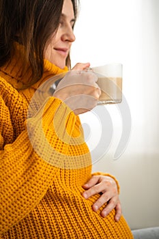 Cute pregnant woman holds in hand a cup of coffee. Concept of a happy pregnancy. Not healthy drinks